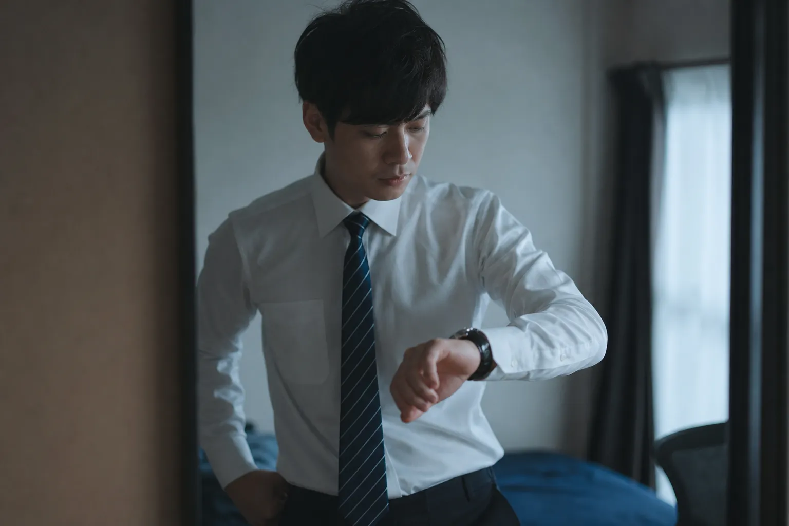 早朝、まだ薄暗い部屋で、ワイシャツ姿の30代の日本人男性が腕時計をちらりと見ながら急いで身支度をしている