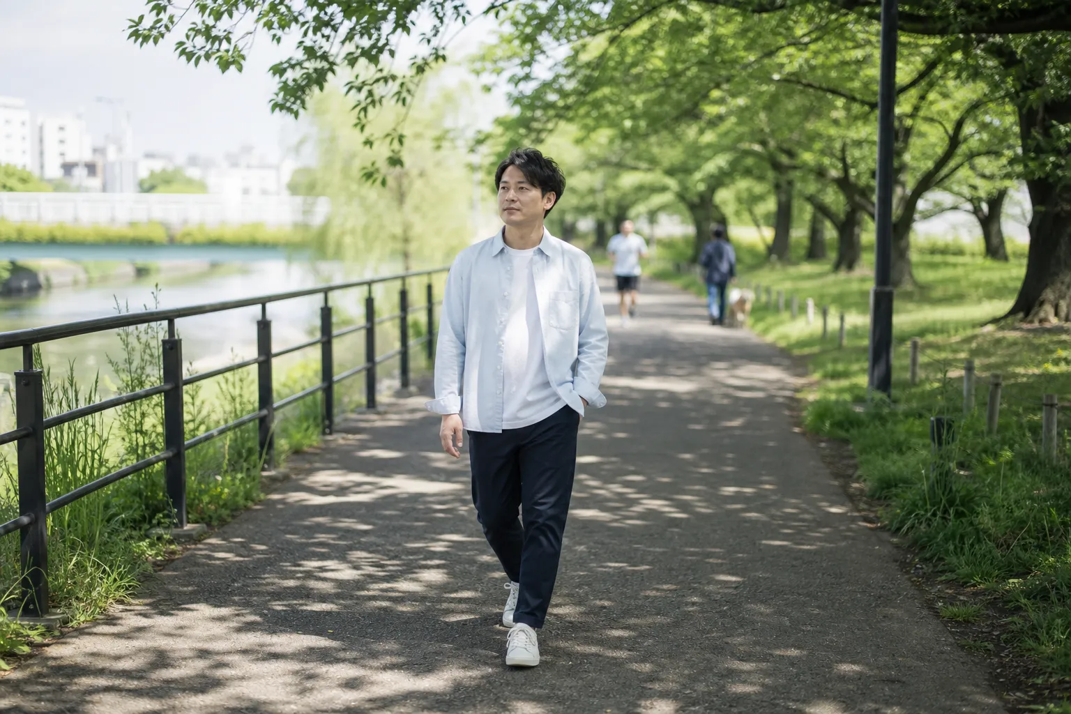 休日の朝、川沿いの遊歩道を歩く30代の日本人男性