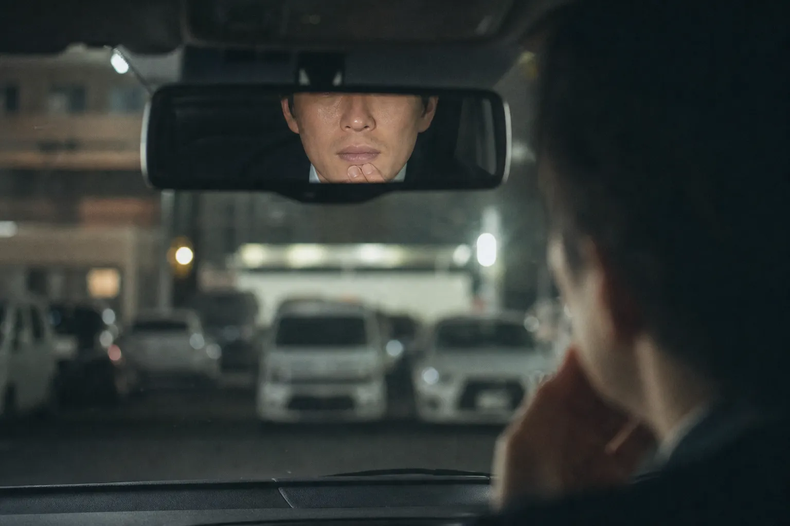 平日の夜、会社の駐車場に停めた車の運転席で、スーツ姿の30代の日本人男性がルームミラーに映る自分の口元をふと確かめている